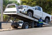 Tow truck loading a white pickup truck on a flatbed trailer beside a roadside