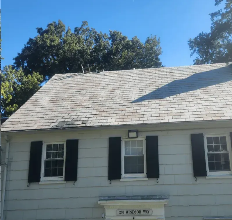 A white house with black shutters, a gray roof, and a clear blue sky, with trees in the background.