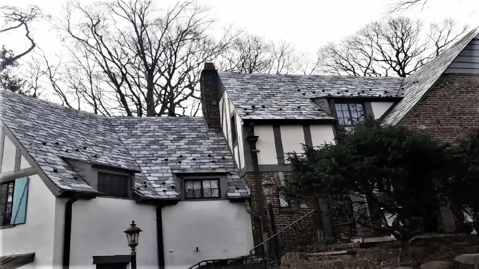 Tudor-style house with slate roof and white and brown exterior. Trees are visible in the background.