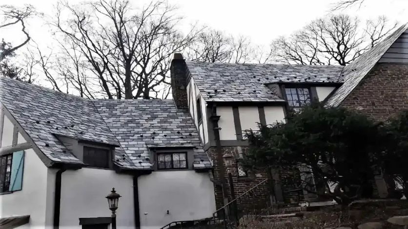 Tudor-style house with slate roof, white stucco walls, and dark wood trim. Trees in background.