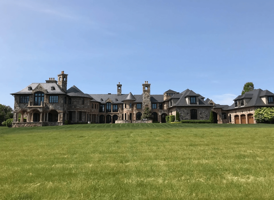 Stone mansion with multiple chimneys and a green lawn under a clear, blue sky.