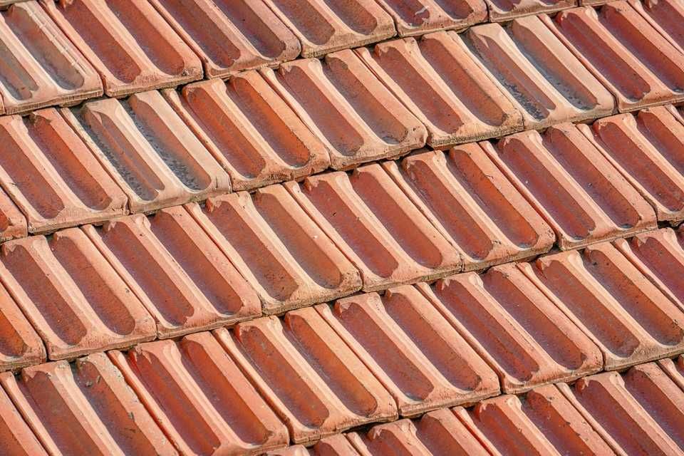 Close-up of a red-brown tile roof, angled, with alternating rows of curved tiles, casting shadows.