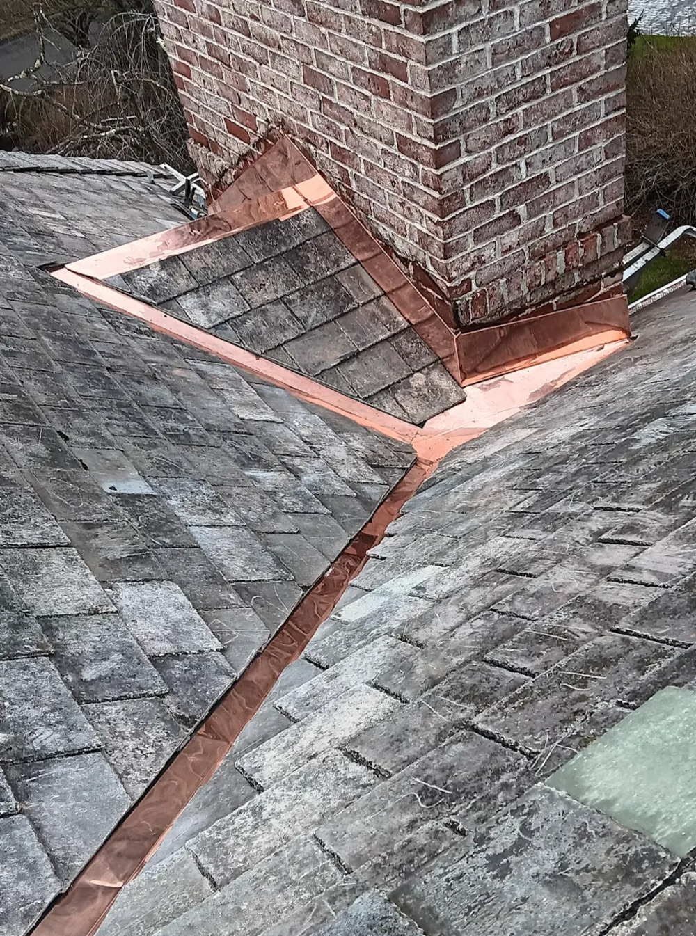 Copper flashing around a brick chimney on a weathered gray slate roof.