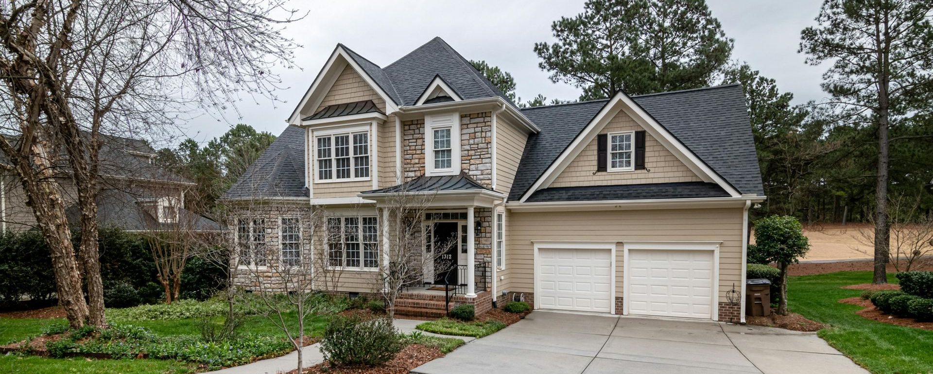 A two-story house with a stone and tan exterior, two-car garage, and a concrete driveway.