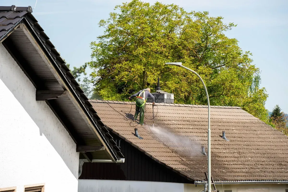 Person pressure washing a tile roof on a sunny day.