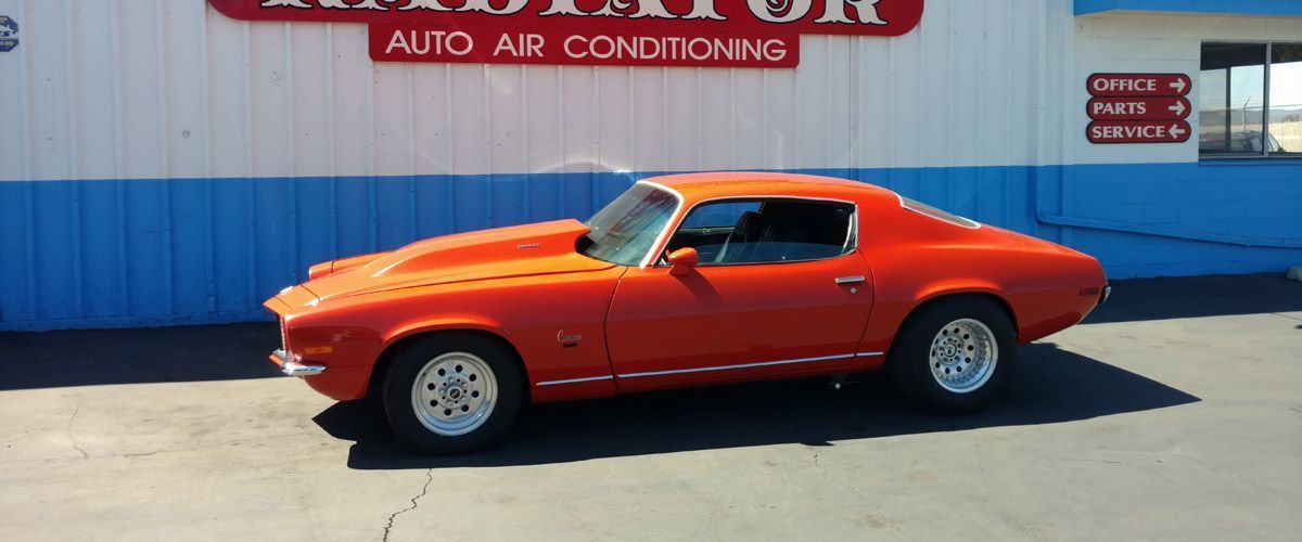 A red car is parked in front of a building that says auto air - conditioning. - Kirk's Radiator & Auto A/C Inc.