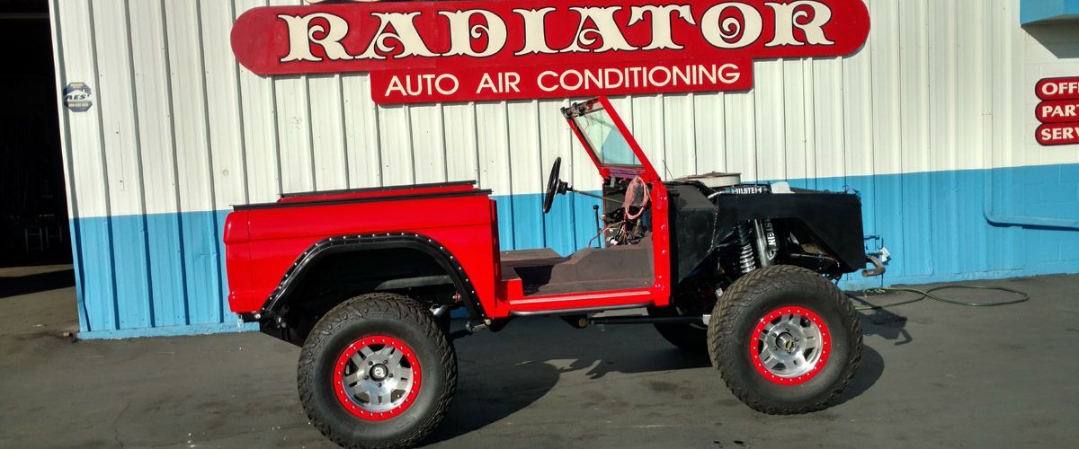 A red jeep is parked in front of a radiator auto air conditioning shop.