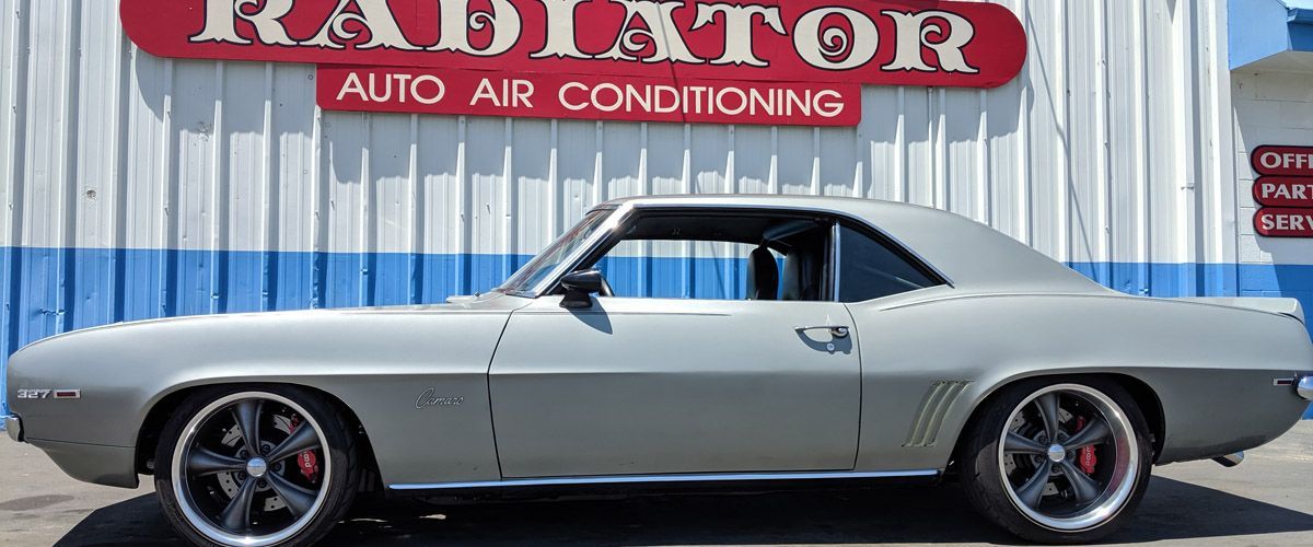 A silver car is parked in front of a building that says radiator auto air conditioning.