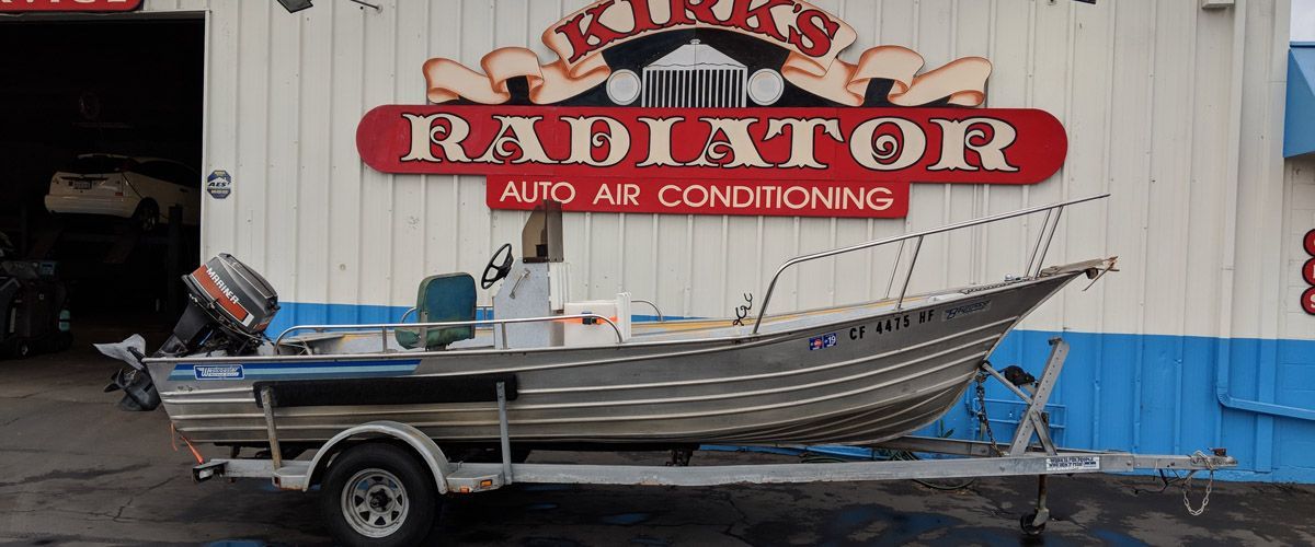 A boat is on a trailer in front of a radiator auto air conditioning store - Kirk's Radiator & Auto A/C Inc.
