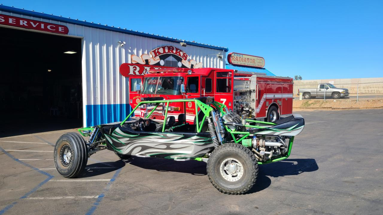 A green and white buggy is parked in front of a garage. | Kirk's Radiator & Auto A/C Inc.