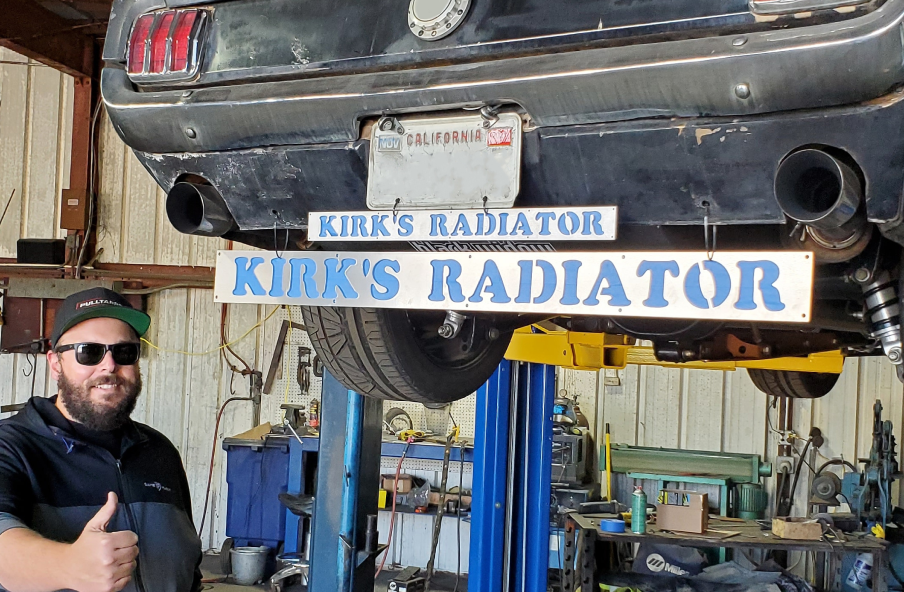A man is giving a thumbs up in front of a car on a lift. | Kirk's Radiator & Auto A/C Inc.