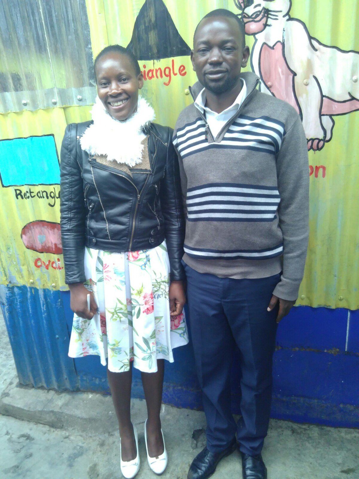 A man and a woman are posing for a picture in front of a wall that says triangle