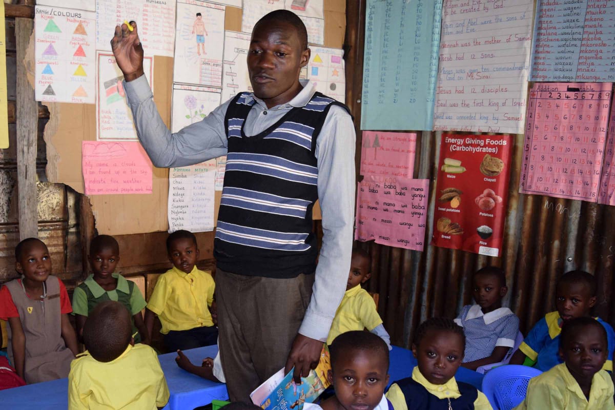 A man is standing in front of a group of children in a classroom.