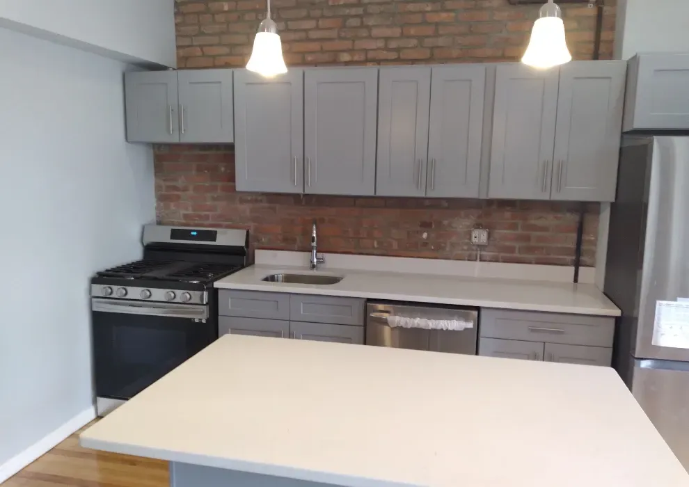 Kitchen with gray cabinets, brick wall, stainless steel appliances, and a white countertop.