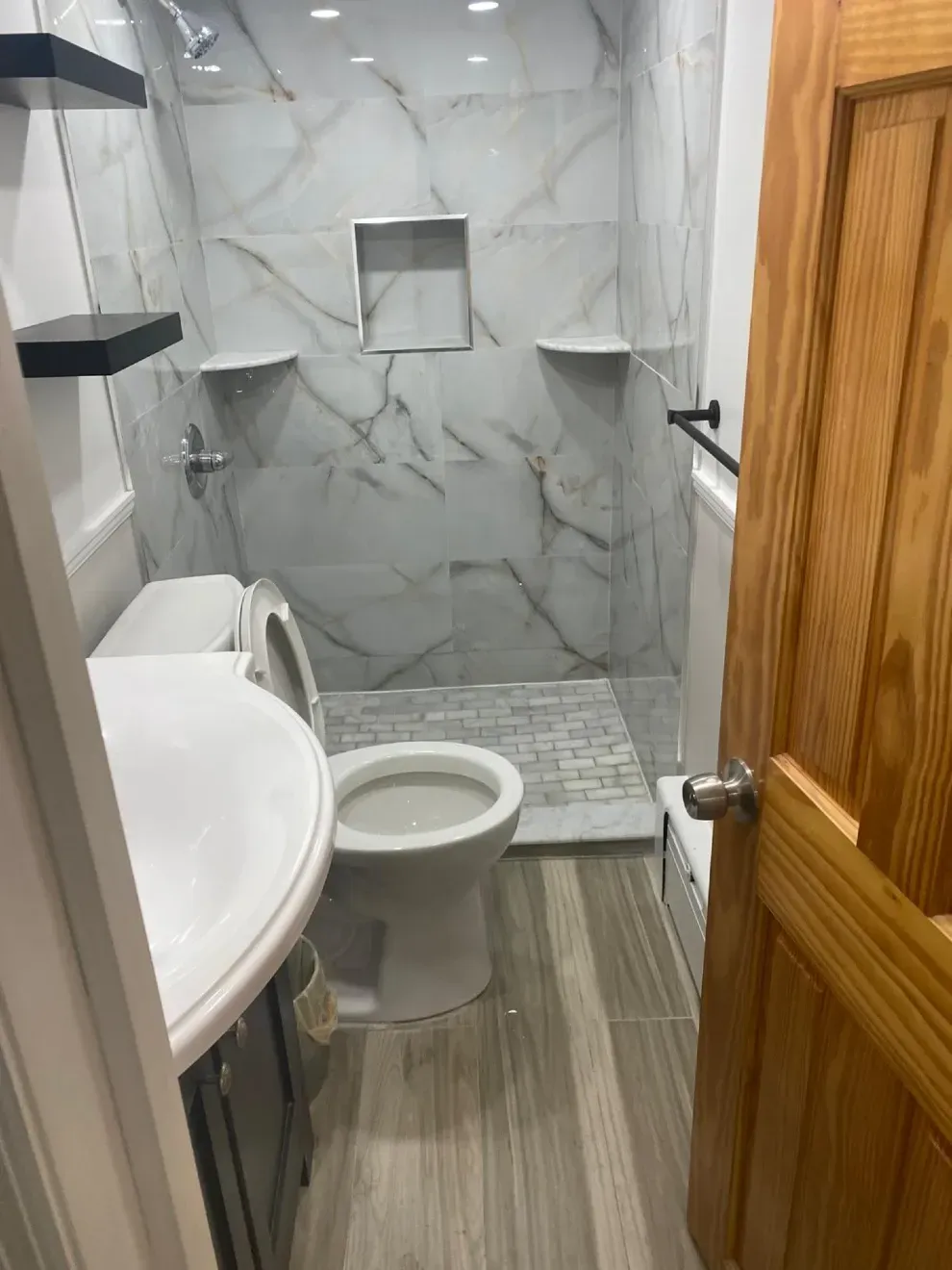 Bathroom with marble tile shower, toilet, and wooden door. Grey and white color scheme.