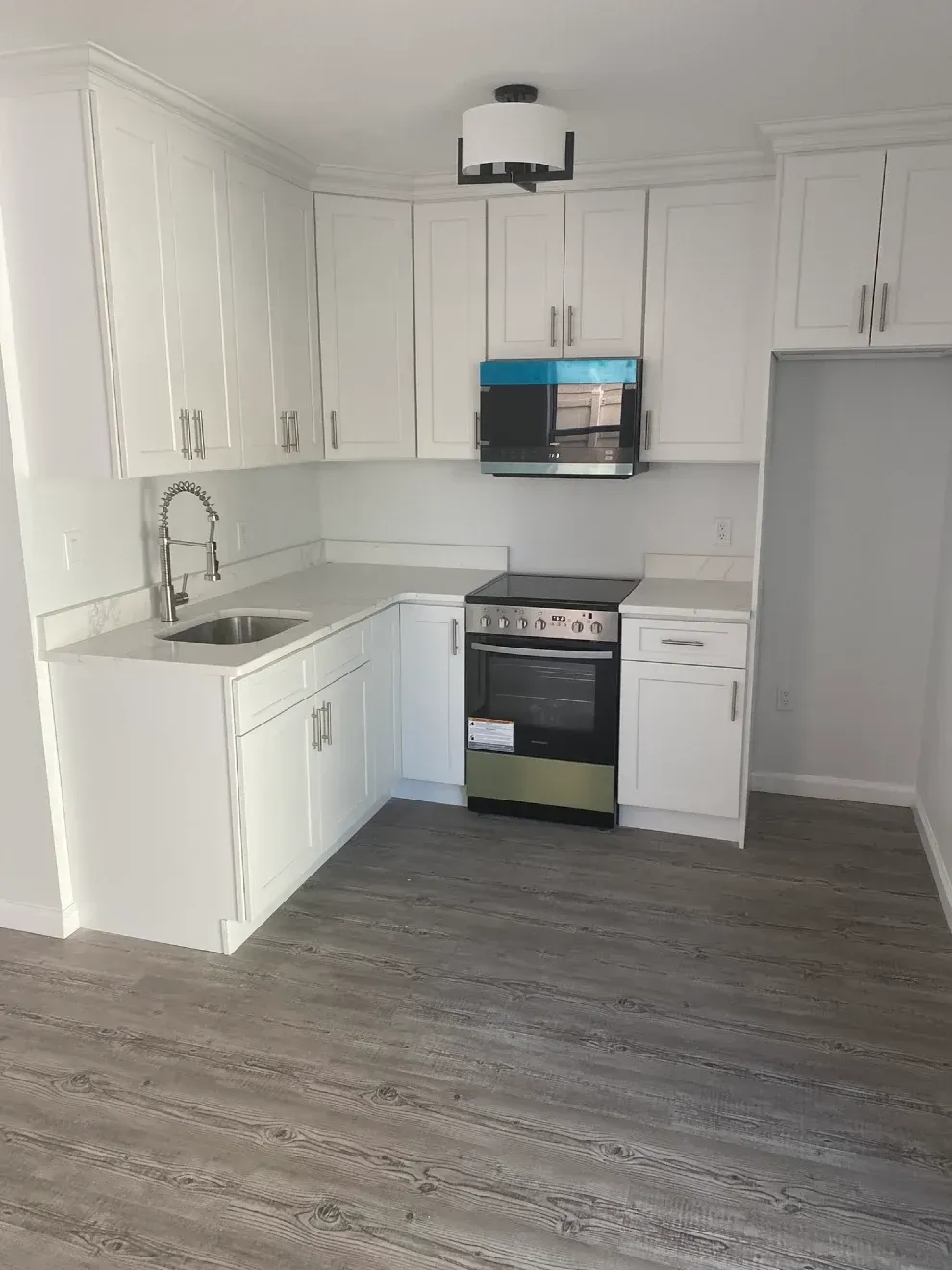 White kitchen with cabinets, countertops, stainless steel appliances, and gray flooring.