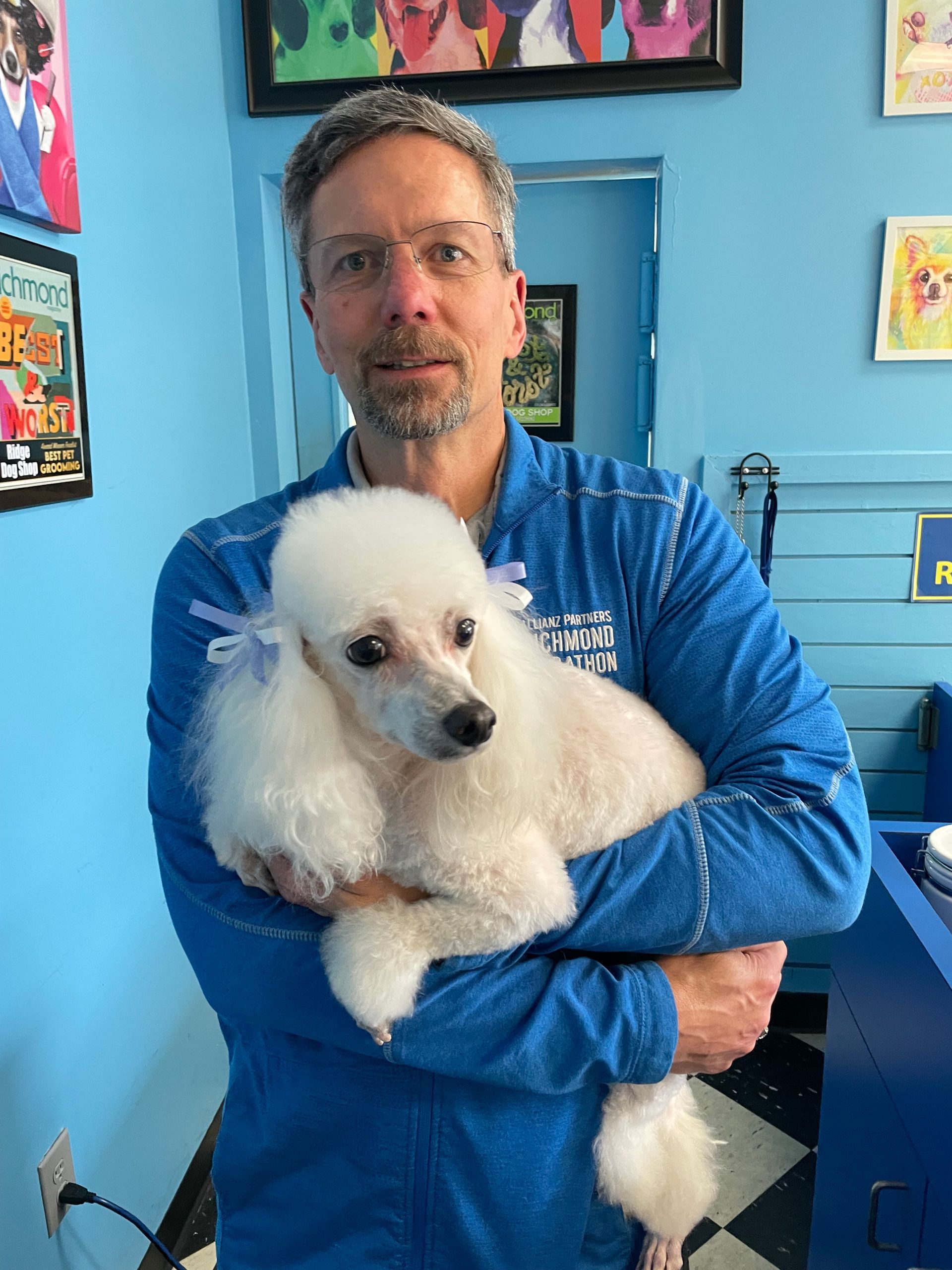 A man in a blue shirt is holding a white poodle.