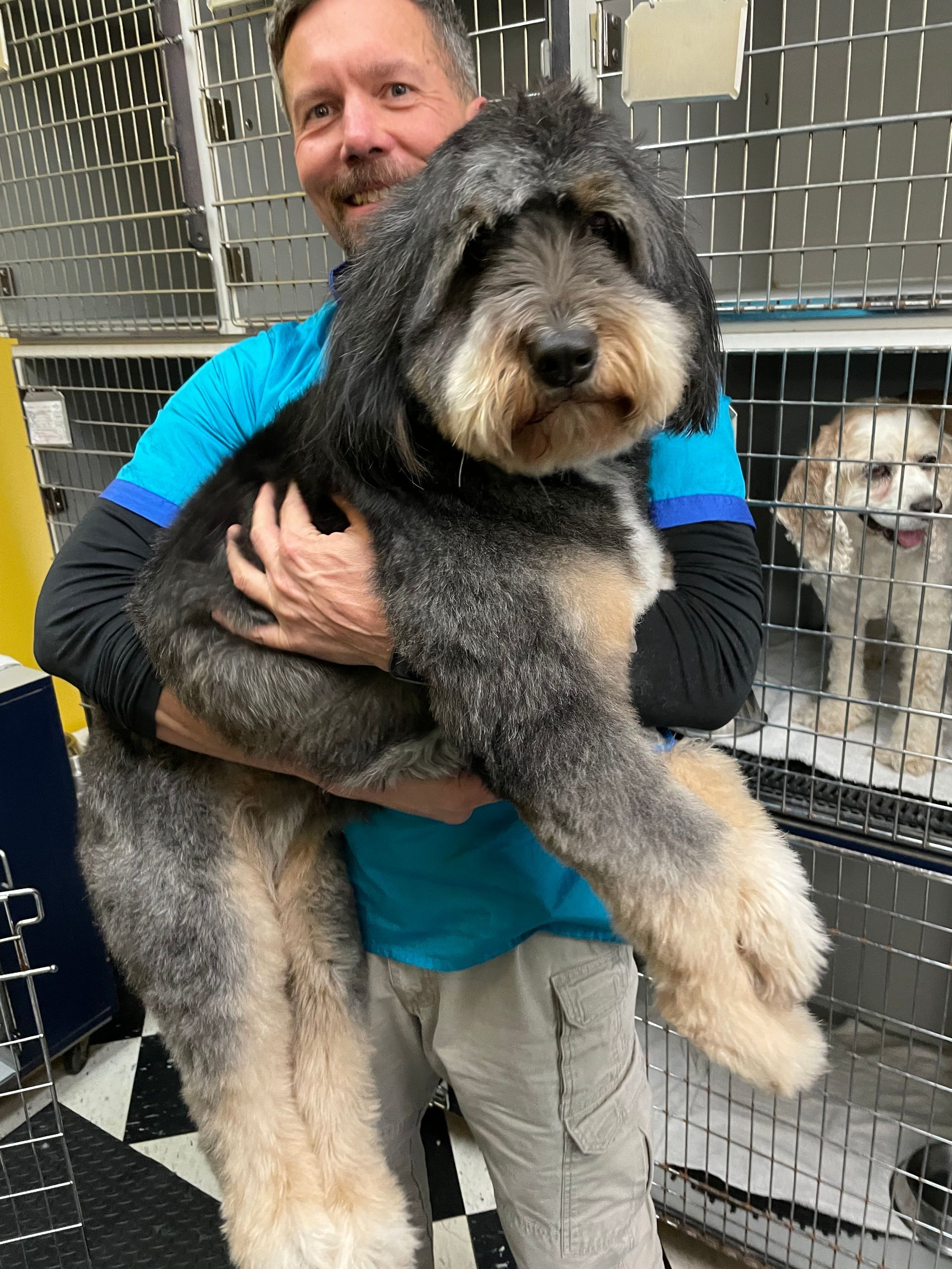 A man is holding a large dog in his arms in front of a cage.