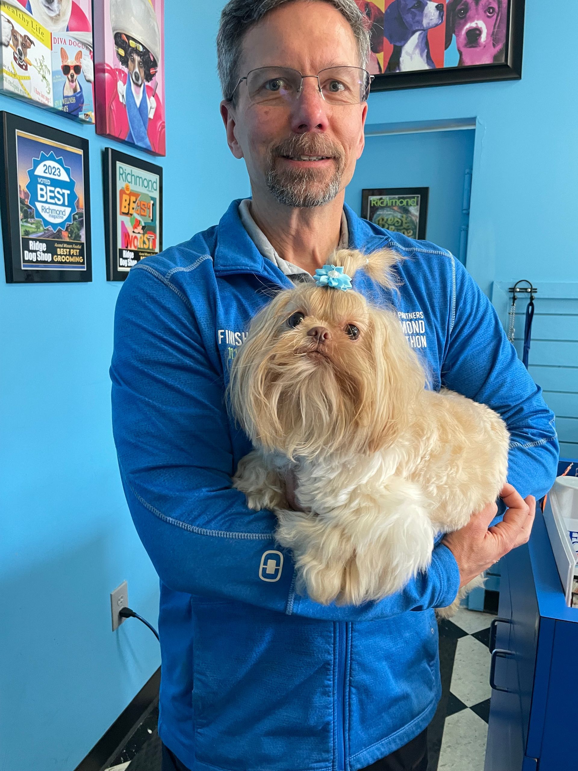 A man in a blue jacket is holding a small dog in his arms.