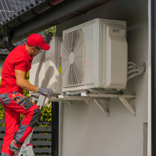 HVAC technician in red uniform installing outdoor air conditioning unit.