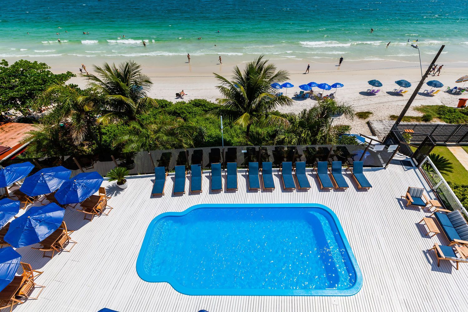 Uma vista aérea de uma piscina cercada por cadeiras e guarda-sóis ao lado de uma praia.