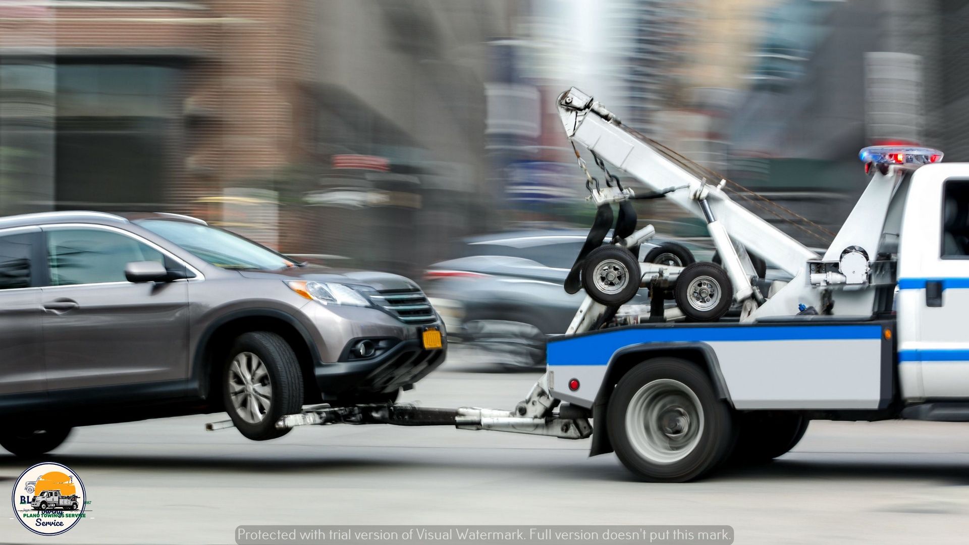 A gray SUV being towed by a white tow truck on a city street.