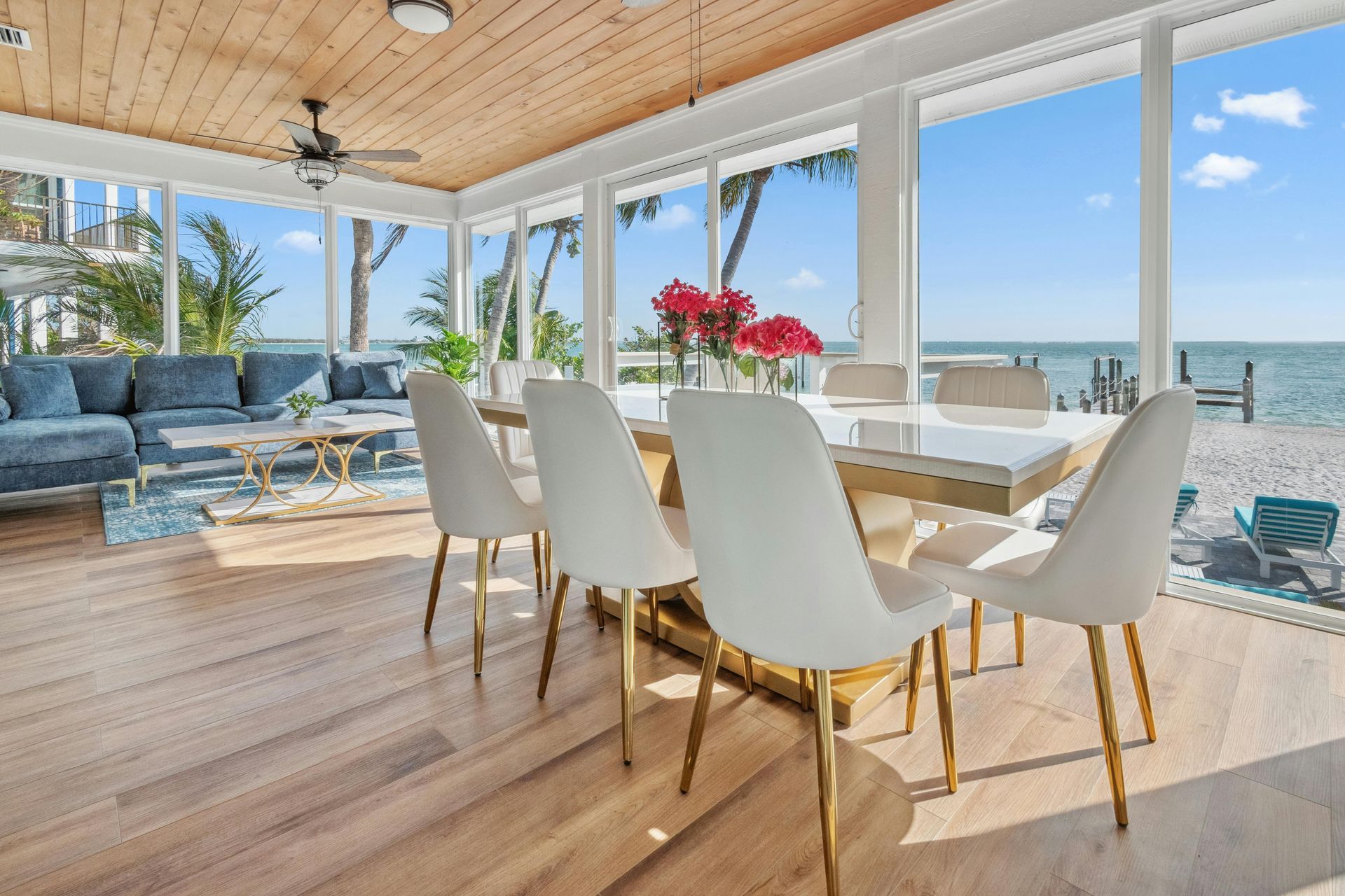 Sunroom with dining table, white chairs, and water view, furnished with a blue sectional couch.