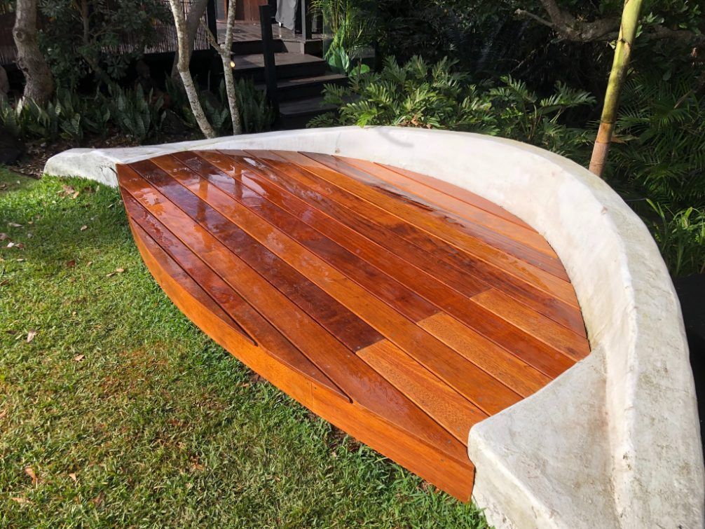 A Wooden Bench in the Shape of a Boat is Sitting in the Grass — Byron Bay Carpentry and Construction In Suffolk Park, NSW