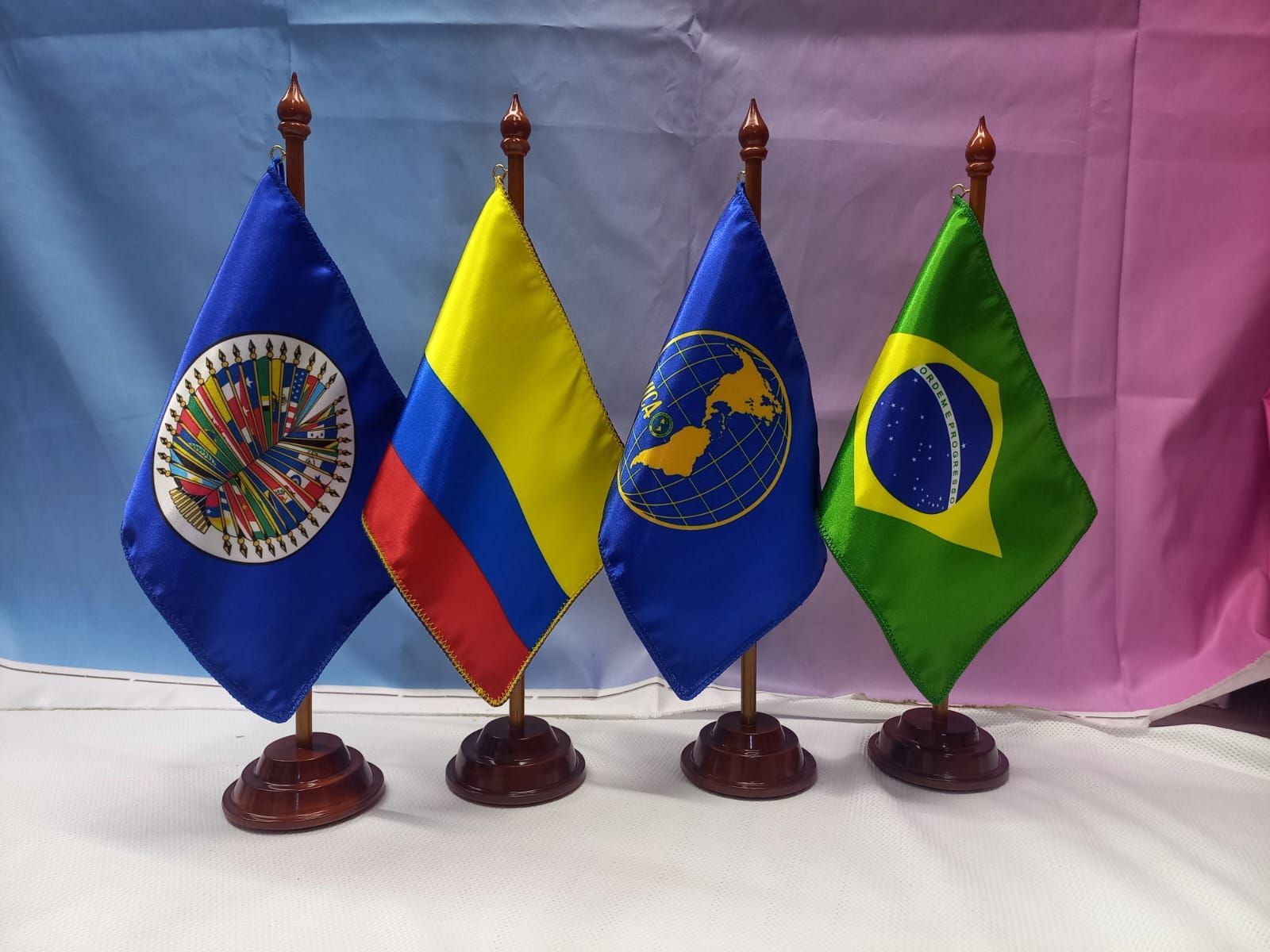 Cuatro pequeñas banderas de escritorio sobre soportes: la de la OEA, la de Colombia y la de Brasil.