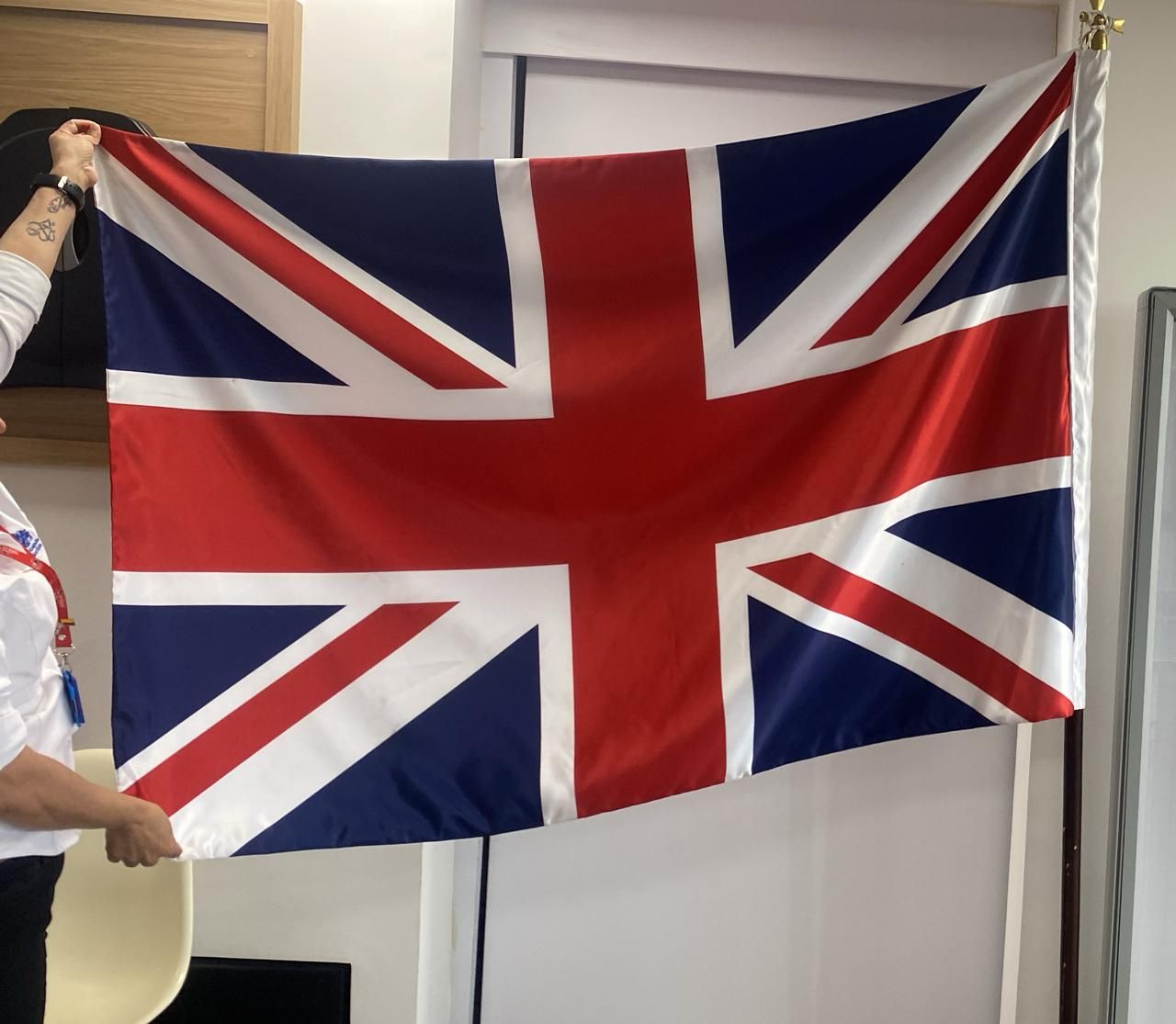 Una gran bandera británica cuelga en el interior de una vivienda, sostenida por una persona en el extremo izquierdo.