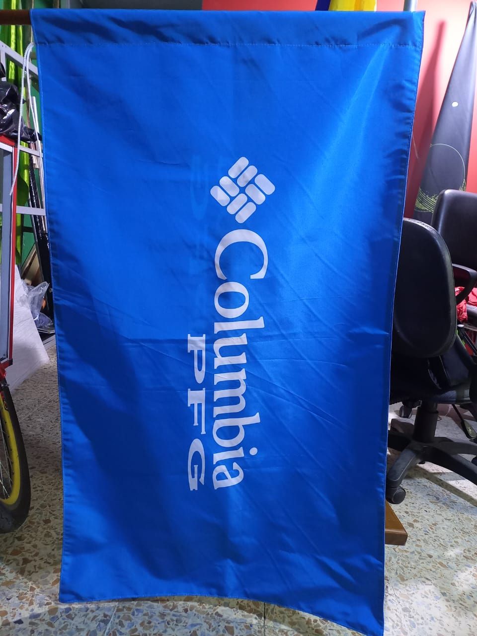 Pancarta azul de Columbia PFG con logotipo blanco colgada al aire libre