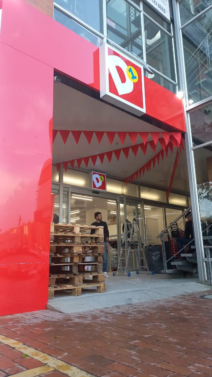 Fachada roja con entrada abierta, banderines y palés en el exterior de una tienda en un edificio moderno.