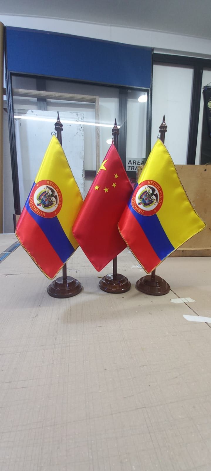 Tres banderas de escritorio ecuatorianas y una bandera roja sobre pequeños soportes en un entorno de oficina.