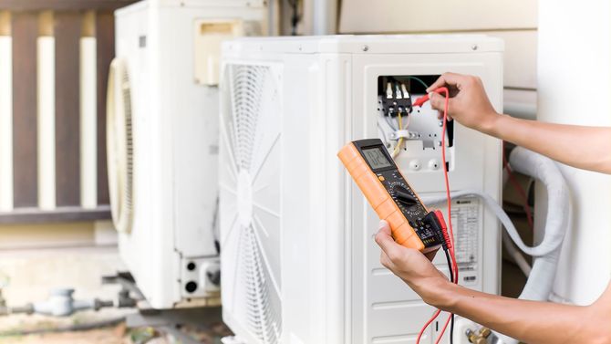 A technician uses a multimeter to test the electrical wiring on the outdoor unit of a residential air conditioner.
