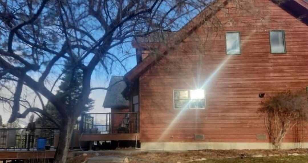 Wooden house exterior with windows, deck, and a tree. Sunny day.