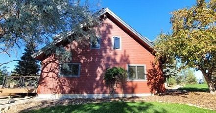 Red-sided house with a gabled roof; windows, deck, and trees are present.