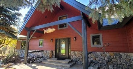 Red cabin with stone base, dark trim, and fish decor above the front door.