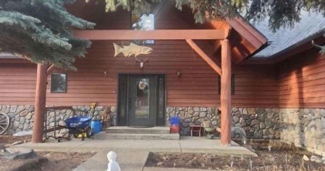 Brown cabin entrance with wooden beams and a stone base, a fish carving above the door.