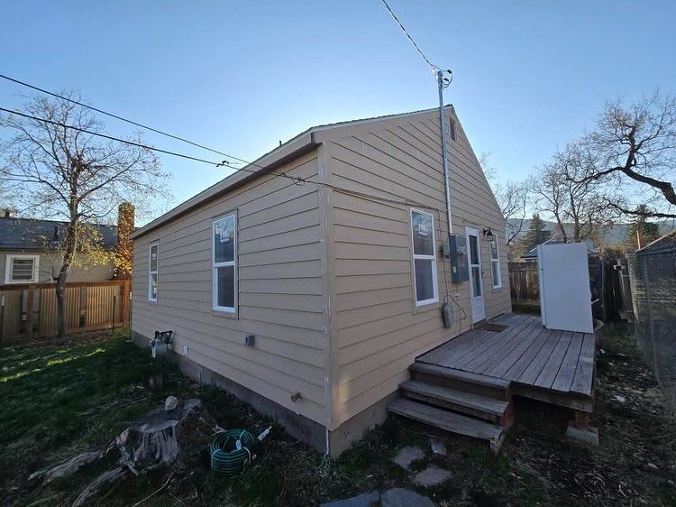 Beige house with a wooden deck, backyard setting under a sunny sky.