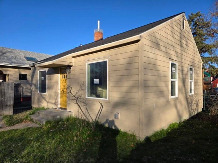 Tan house with black roof, white-framed windows, and a yellow door; blue sky and grass.