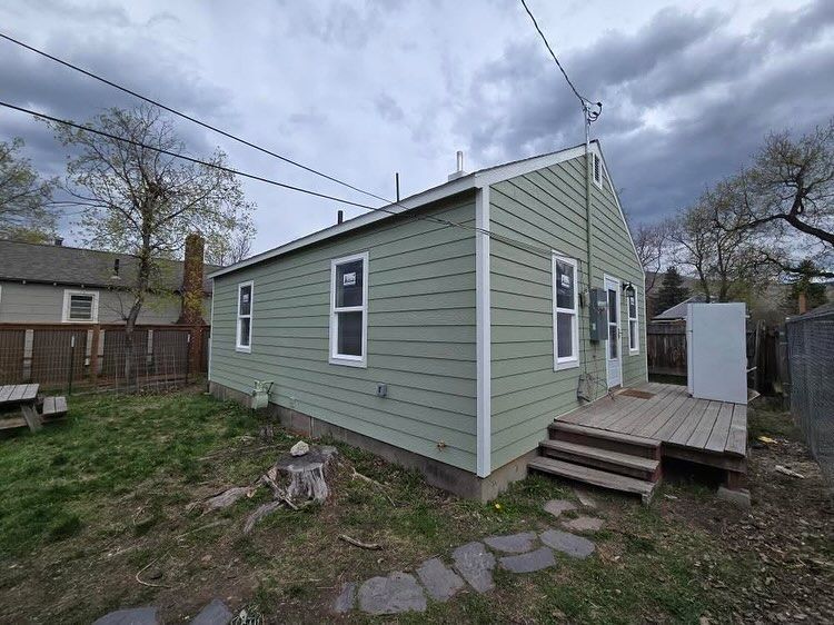 A green house with white trim and windows, a small wooden deck, and a cloudy sky.