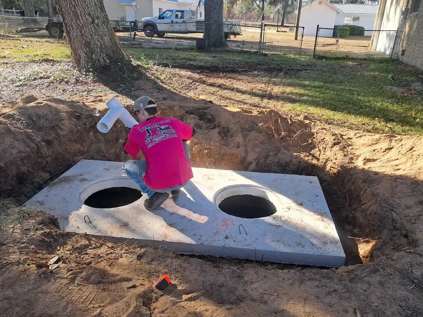 Child in a bright pink shirt kneeling on a concrete slab with two large holes in a dirt yard.
