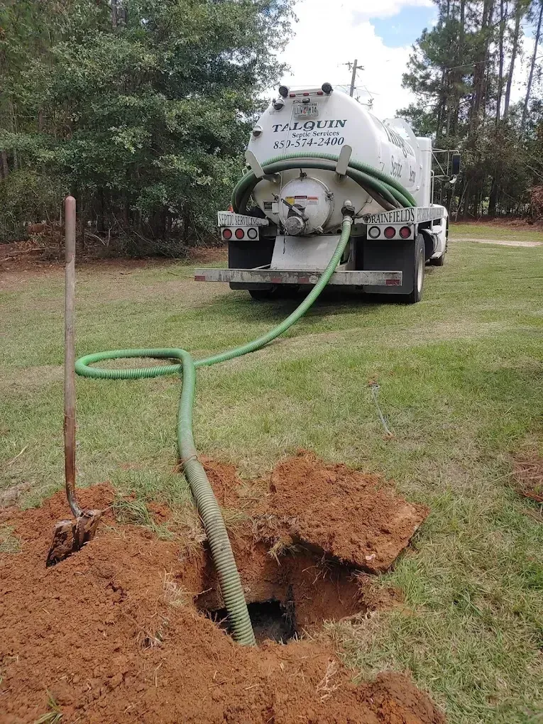 Sewer vacuum truck clearing a clogged pipe, with a green hose leading into a hole in the ground.