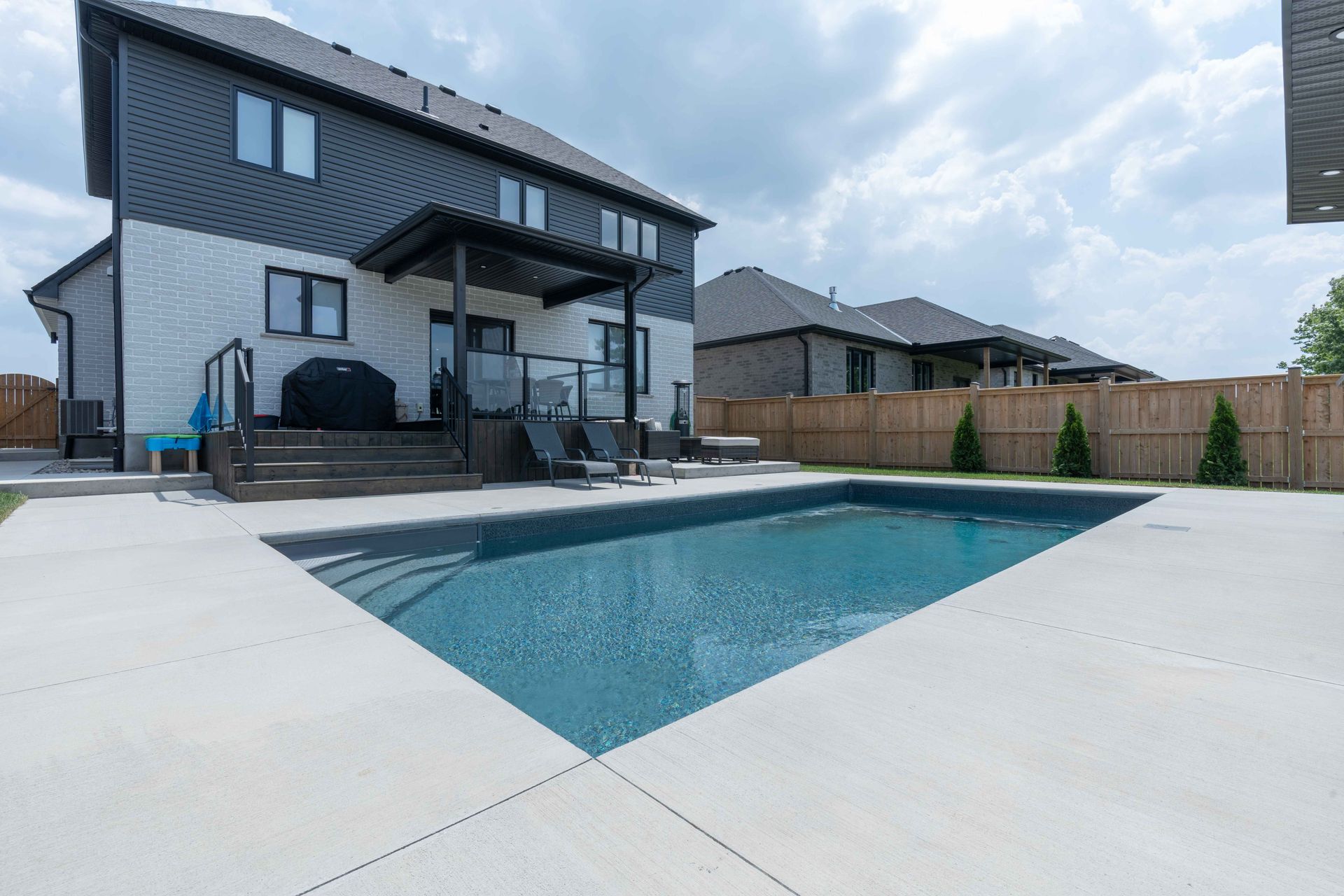Backyard with modern two-story house and covered patio beside an empty swimming pool