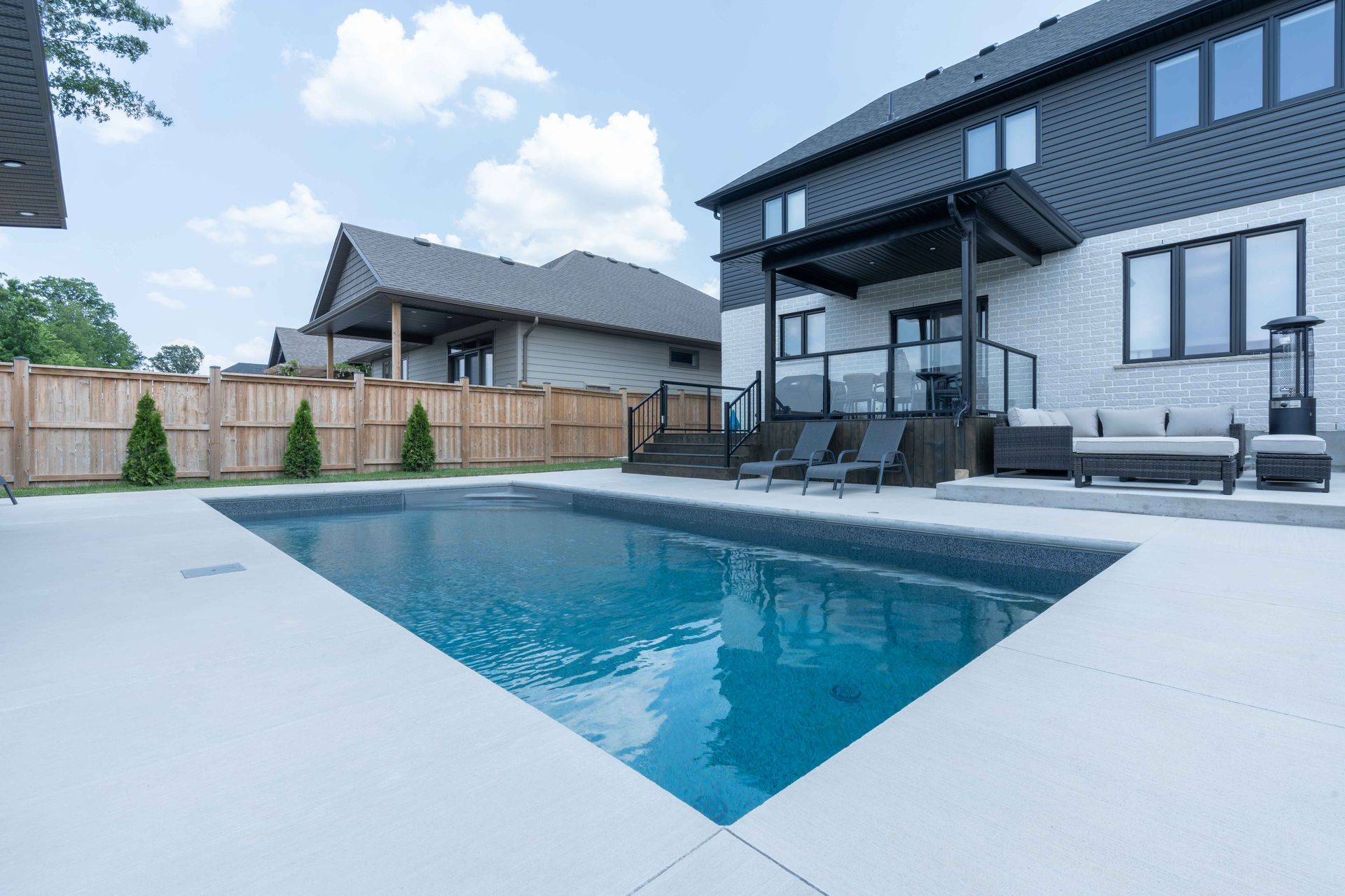 Modern backyard with a rectangular swimming pool beside a two-story house and patio seating area