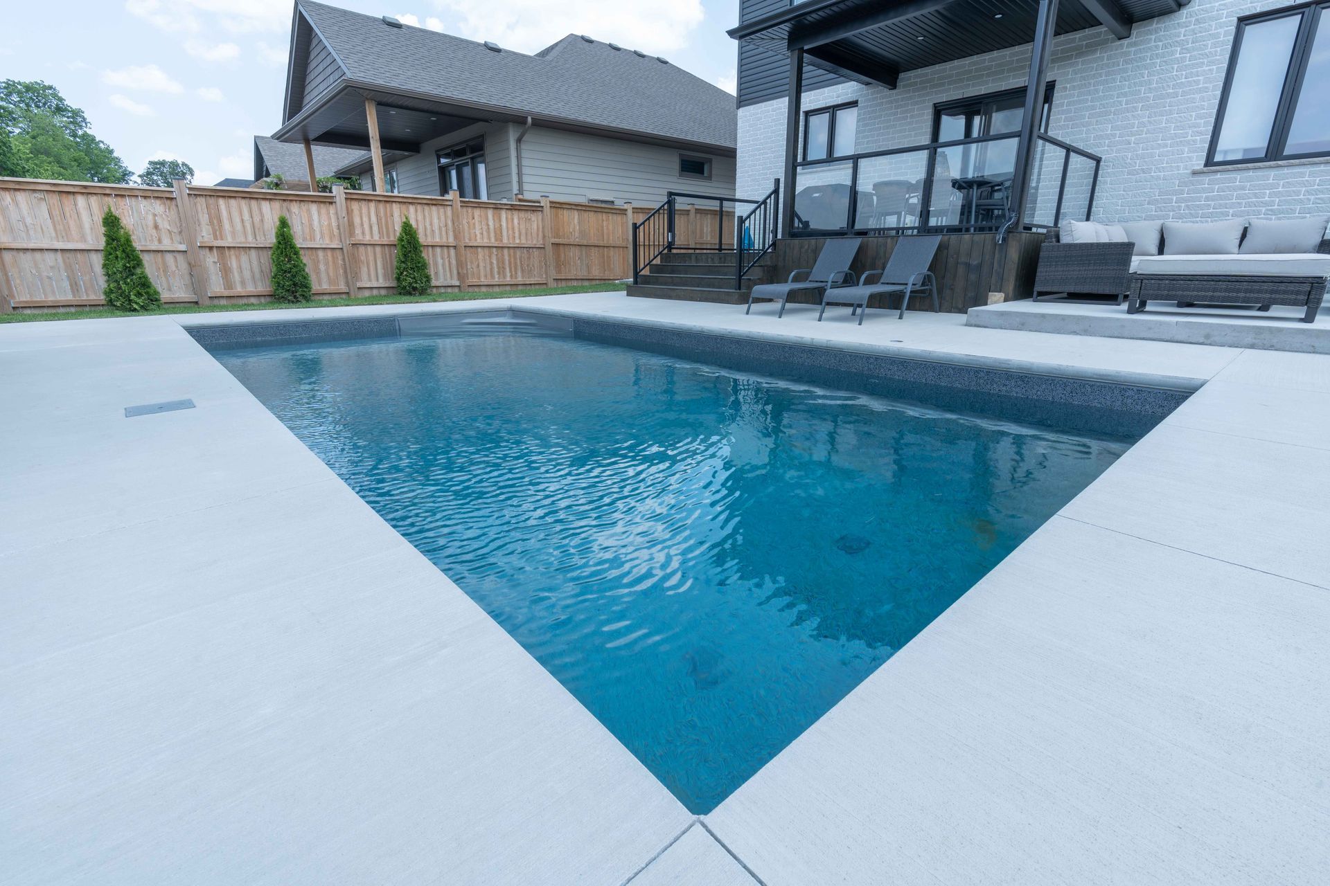 Modern backyard with a triangular in-ground pool, patio seating, and a fenced suburban home.