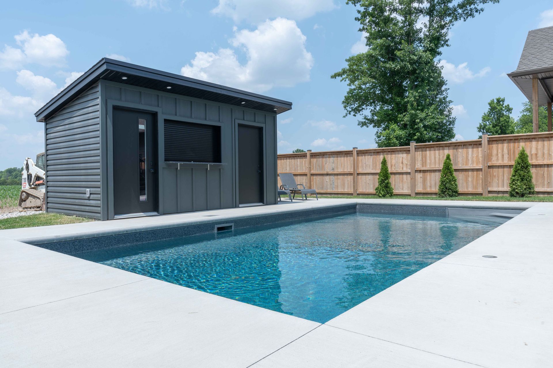 Backyard swimming pool beside a gray shed under a blue sky