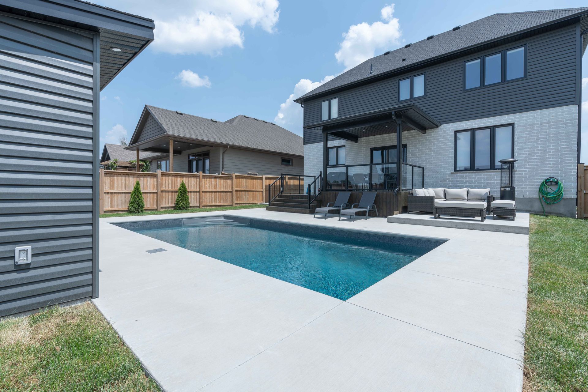 Modern backyard patio with rectangular swimming pool and two-story gray house.