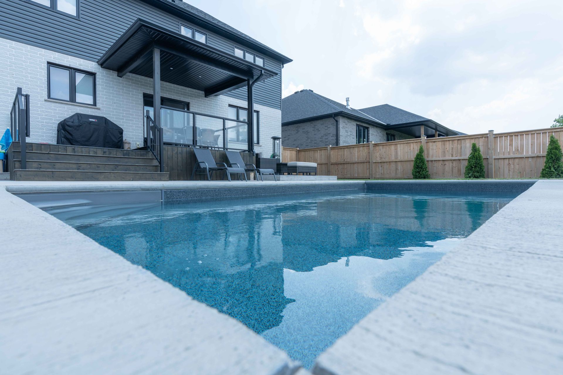 Modern backyard patio with a geometric swimming pool beside a dark gray house