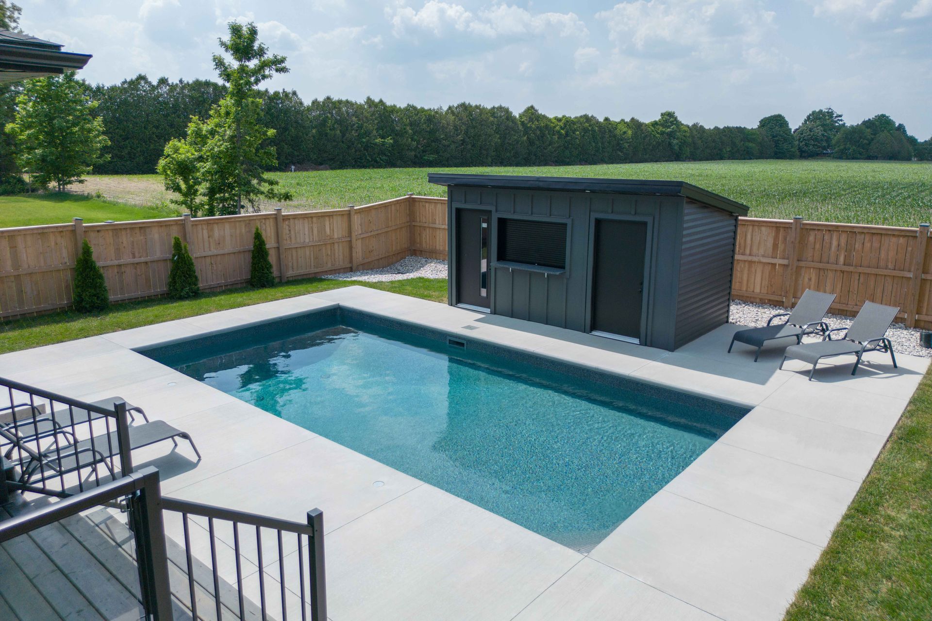 Backyard in-ground pool beside a small pool house, with lounge chairs and a fenced yard